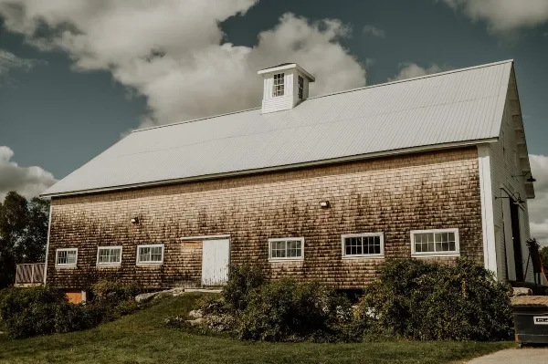 Exterior view of a large wooden barn with a white metal roof and cupola, situated on a grassy estate.