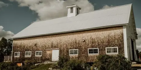 Exterior view of a large wooden barn with a white metal roof and cupola, situated on a grassy estate.