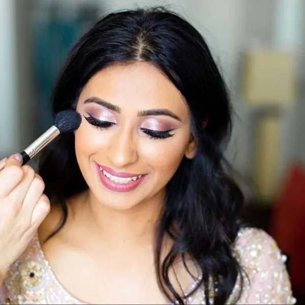 A makeup artist applying eye makeup to a smiling woman with dark hair.