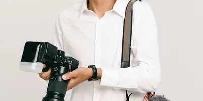 A man in a white shirt holding a professional camera with a flash unit and a second camera with a microphone attached.