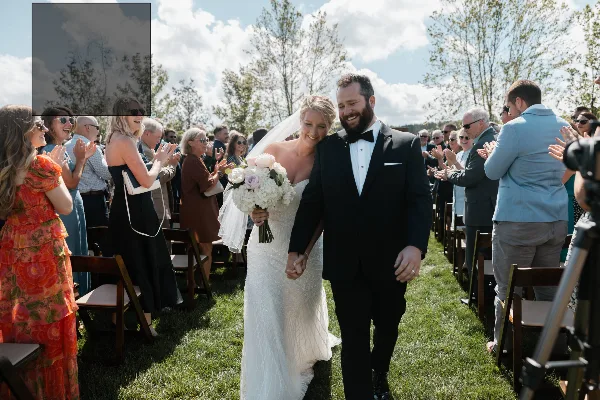 A bride and groom walking down the aisle during an outdoor wedding ceremony with guests seated on either side.
