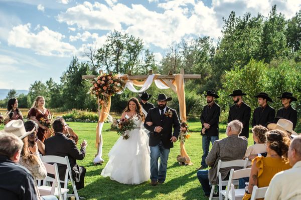 A bride and groom walking down the aisle during an outdoor wedding ceremony at a rustic venue.