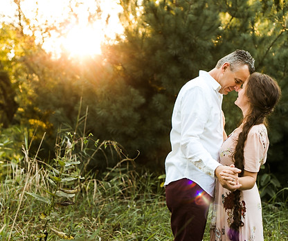 A couple embracing outdoors in a natural setting with sunlight filtering through trees.