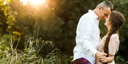 A couple embracing outdoors in a natural setting with sunlight filtering through trees.