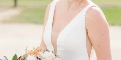 A smiling bride in a white dress holding a bouquet of flowers, showcasing her styled hair and makeup.