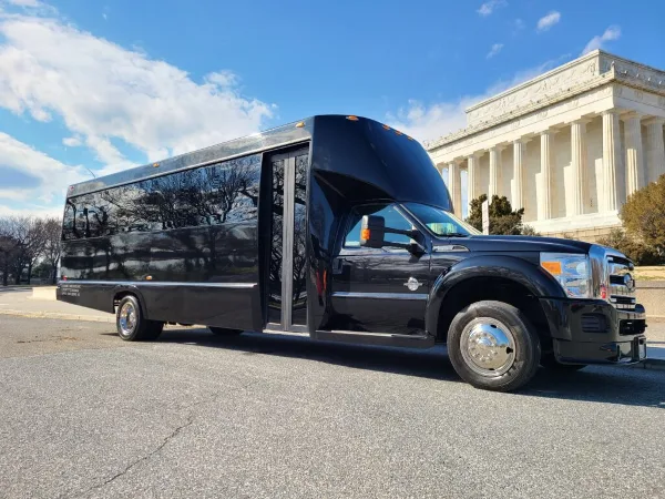 A black Bayside Limousine shuttle bus parked on a street with a classical building in the background.