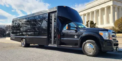 A black Bayside Limousine shuttle bus parked on a street with a classical building in the background.