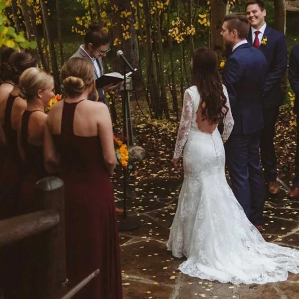 A bride and groom exchanging vows during an outdoor wedding ceremony in a wooded area.