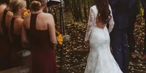 A bride and groom exchanging vows during an outdoor wedding ceremony in a wooded area.