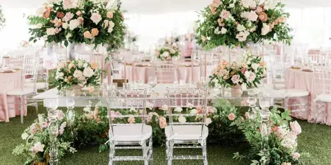 A luxury wedding reception table setting with large floral arrangements and clear chairs.