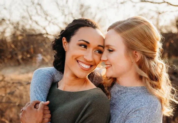 Two women with styled hair and makeup embracing outdoors.