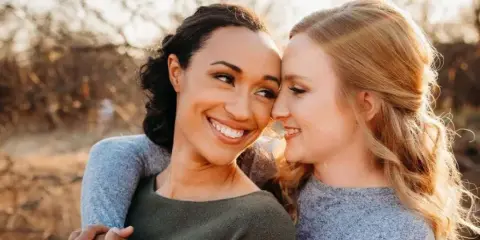 Two women with styled hair and makeup embracing outdoors.