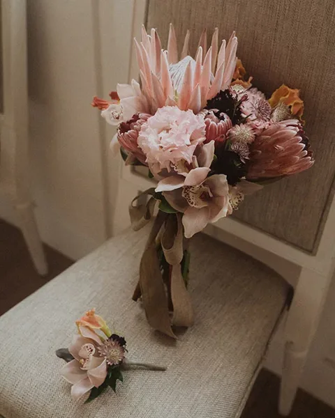 A pink and white bridal bouquet with a matching boutonniere resting on a beige chair.