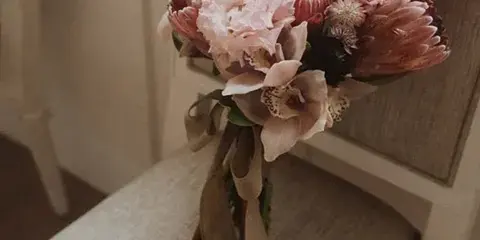 A pink and white bridal bouquet with a matching boutonniere resting on a beige chair.