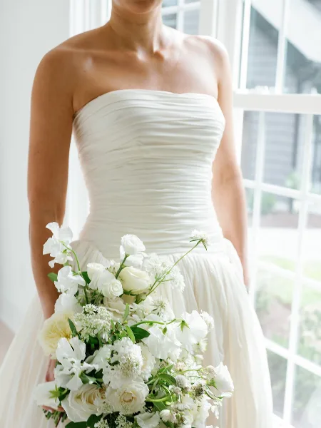 A bride in a white strapless wedding dress holding a bouquet of white flowers.