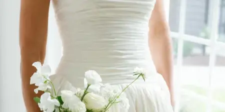 A bride in a white strapless wedding dress holding a bouquet of white flowers.
