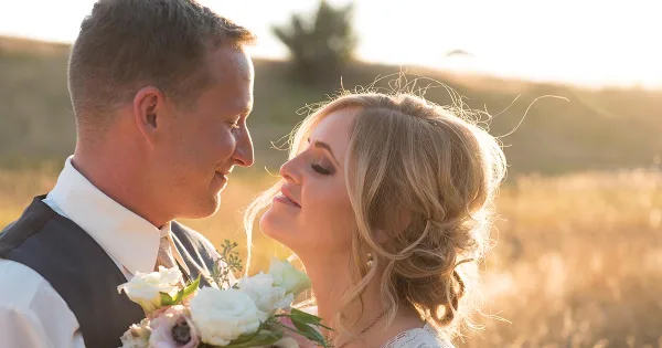 A bride and groom in wedding attire sharing an intimate moment outdoors in a grassy field with golden hour lighting.