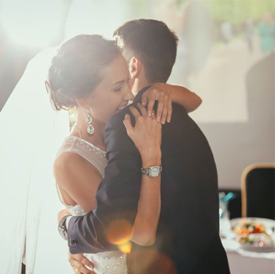 A bride and groom dancing together at a wedding reception with a decorated table in the background.