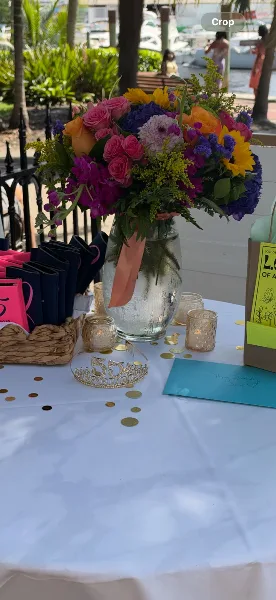 A large, colorful floral arrangement featuring roses, hydrangeas, and sunflowers in a glass vase on a table.