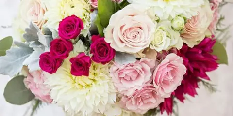 A close-up photograph of a floral bouquet containing pink and white roses, dahlias, and greenery, with the word 'Wedding' printed on a yellow banner at the bottom.