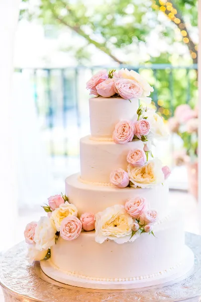 A four-tier white wedding cake decorated with cascading pink and white roses on a silver stand.