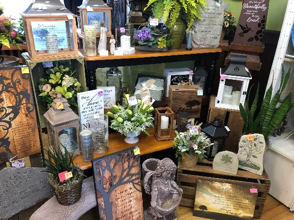 Interior view of a floral shop displaying flower arrangements, potted plants, and decorative gifts on wooden shelves.