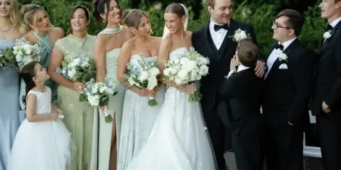 A wedding party, including the bride and groom, posing for a group portrait outdoors.