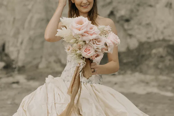 A bride in a white wedding dress holding a bouquet of pink roses and white flowers.