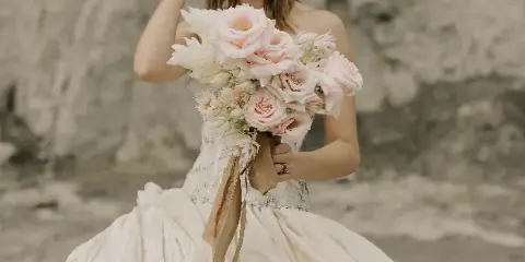 A bride in a white wedding dress holding a bouquet of pink roses and white flowers.