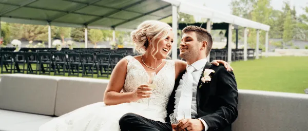 A bride and groom sitting together at a wedding reception, smiling and holding drinks.