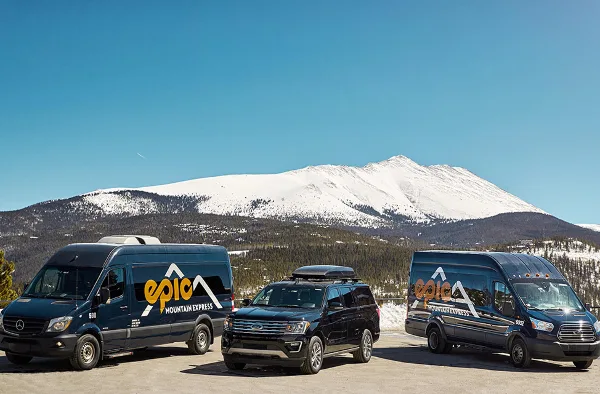 A fleet of Epic Mountain Express vans and SUVs parked in front of a snowy mountain.