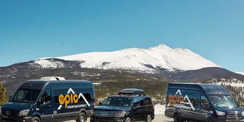 A fleet of Epic Mountain Express vans and SUVs parked in front of a snowy mountain.
