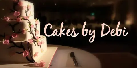 A three-tiered white wedding cake decorated with pink flowers and dark branches, sitting on a table with a cake knife.