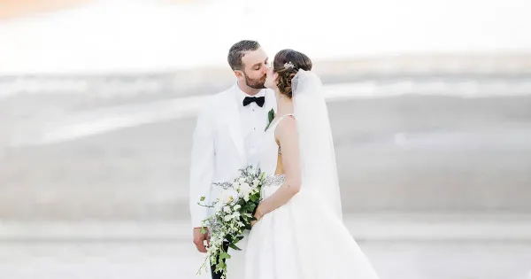 A bride and groom kissing on a beach with the ocean in the background.