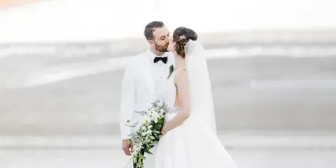 A bride and groom kissing on a beach with the ocean in the background.