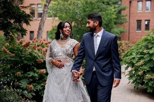 A bride and groom holding hands and smiling at each other outdoors.