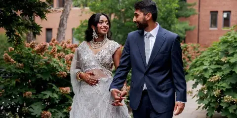 A bride and groom holding hands and smiling at each other outdoors.
