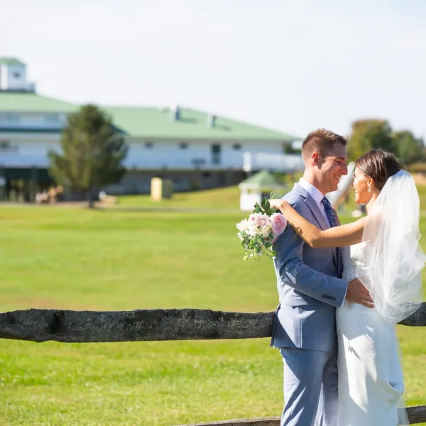 A bride and groom standing outdoors on a golf course with a large white building in the background.