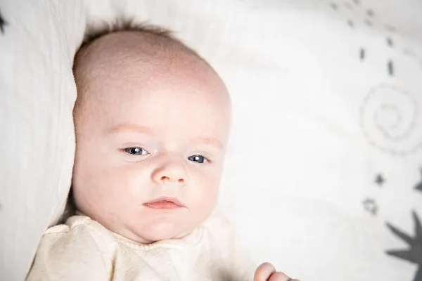 A professional close-up portrait of a newborn baby lying on a white textured blanket with a soft-focus background.