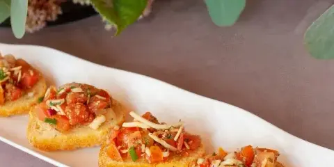 A white platter of bruschetta topped with tomatoes and cheese, set against a backdrop of a vibrant floral arrangement.