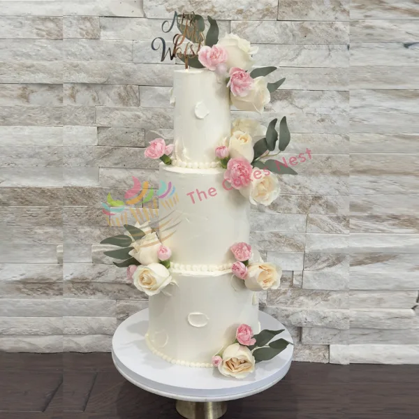A three-tier white wedding cake decorated with pink and white roses and a Mr & Mrs topper.