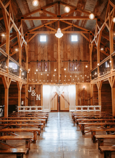 Interior view of a wooden barn wedding venue with rows of chairs and string lights.