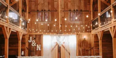 Interior view of a wooden barn wedding venue with rows of chairs and string lights.