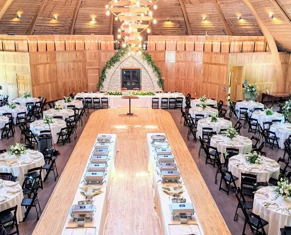 Interior of a rustic timber frame barn venue set up for a wedding reception with round tables and a dance floor.