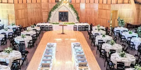 Interior of a rustic timber frame barn venue set up for a wedding reception with round tables and a dance floor.