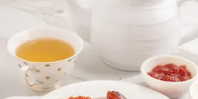 A plate of split scones topped with cream and jam, served with a cup of tea and a white ceramic teapot.