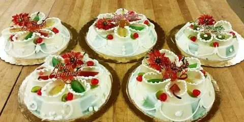 Five decorated Italian specialty cakes with white icing, candied fruit, and red flowers arranged on a wooden table.