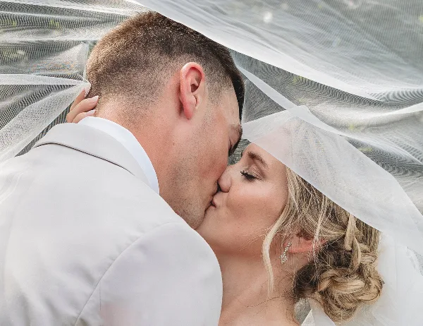 A bride and groom kissing under a white wedding veil.