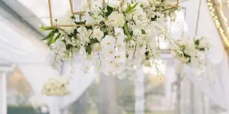 Hanging geometric floral chandeliers and long white table centerpieces in a wedding tent.