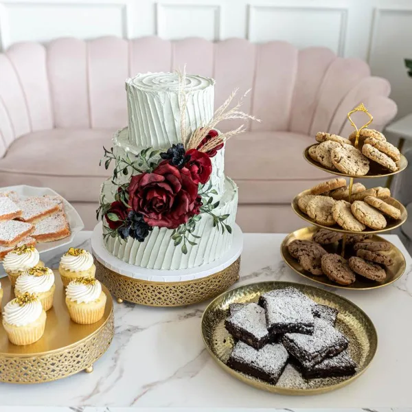 A wedding dessert table featuring a tiered white cake with floral decorations, a stand of cupcakes, a tiered stand of cookies, and a plate of brownies.